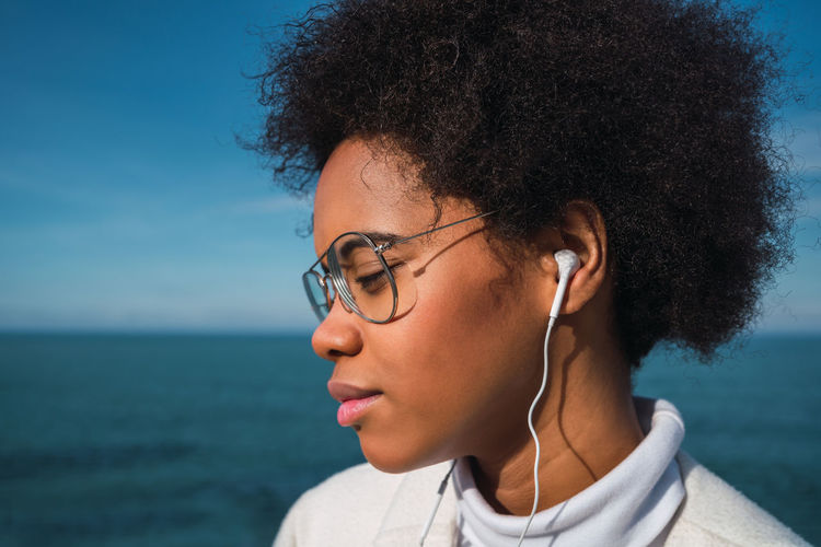 Close-up of young woman with curly hair listening music through headphones