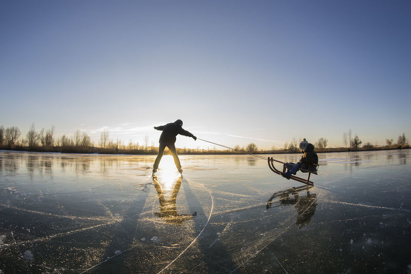 Men fishing on lake against clear sky