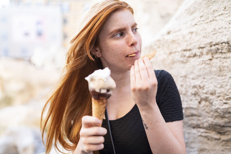 Ginger woman eating biscuit from ice cream cone on street