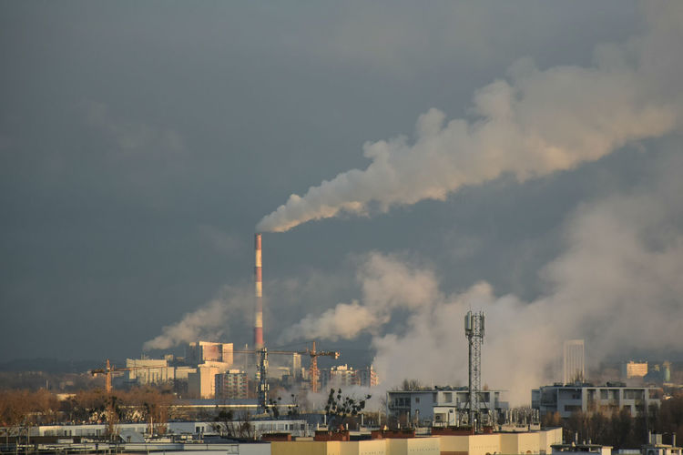Smoke emitting from factory against cloudy sky
