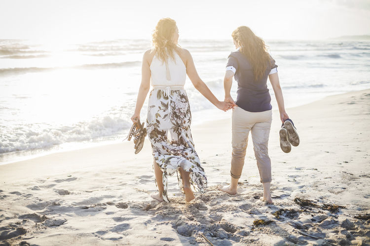 Rear view of women holding hands while walking at beach