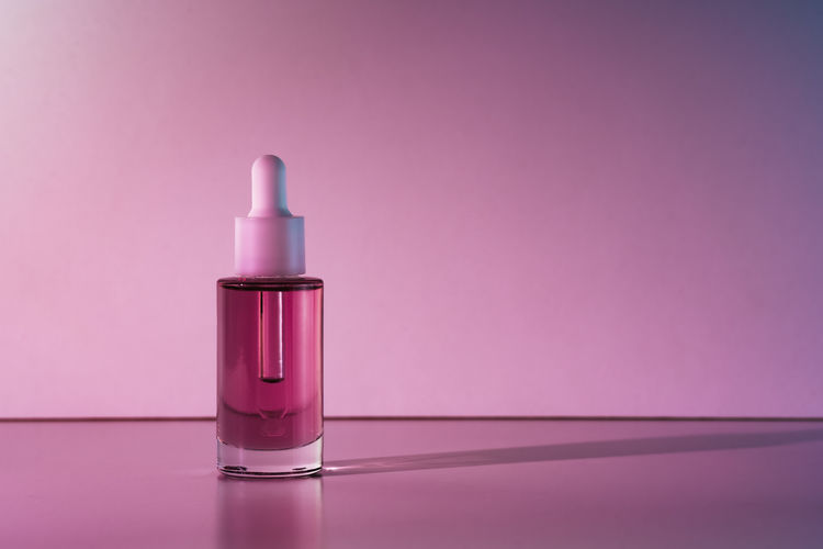 Pink face oil in glass bottle with white pipette dropper cap.
