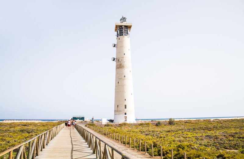 People walking on road by lighthouse against clear sky