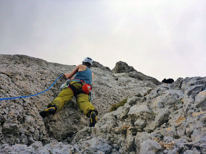 Rear view of man climbing rock on mountain against sky