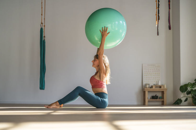 Woman exercising with fitness ball sitting in yoga studio