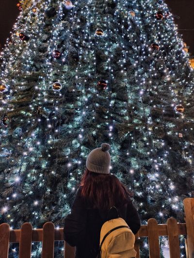 Rear view of woman standing against christmas tree at night