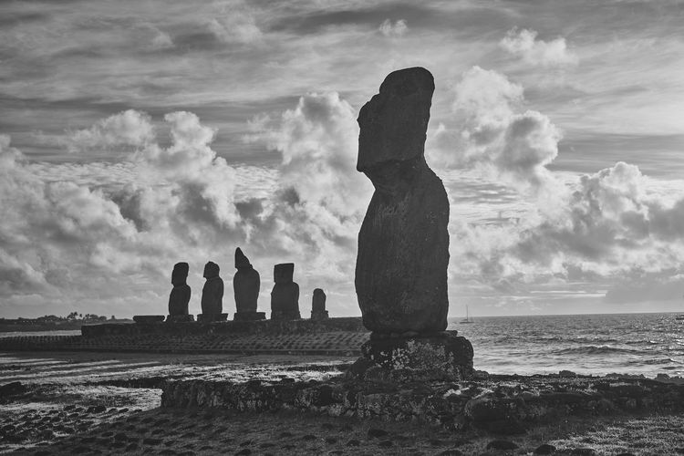 Panoramic view of moai statues against cloudy sky