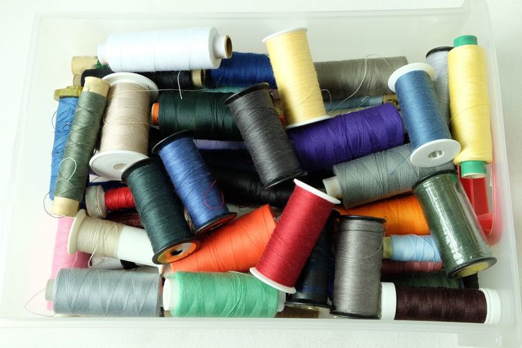 High angle view of colorful thread spools in container on white background