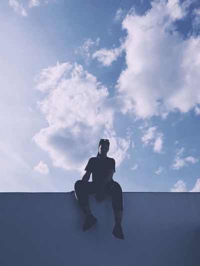 Low angle view of silhouette woman sitting on railing against sky