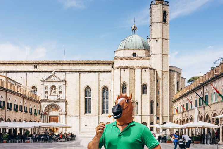 Horse man standing in the middle of the historic square of ascoli piceno eating a fried olive 