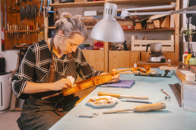 Luthier polishing and repairing violin at desk in workshop