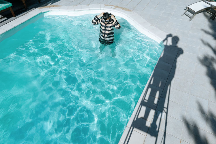 High angle view of man wearing raincoat while standing in swimming pool during sunny day
