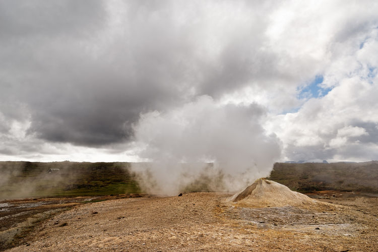 Wide volcanic landscape with a small mud crater and steam blown sideways by the wind