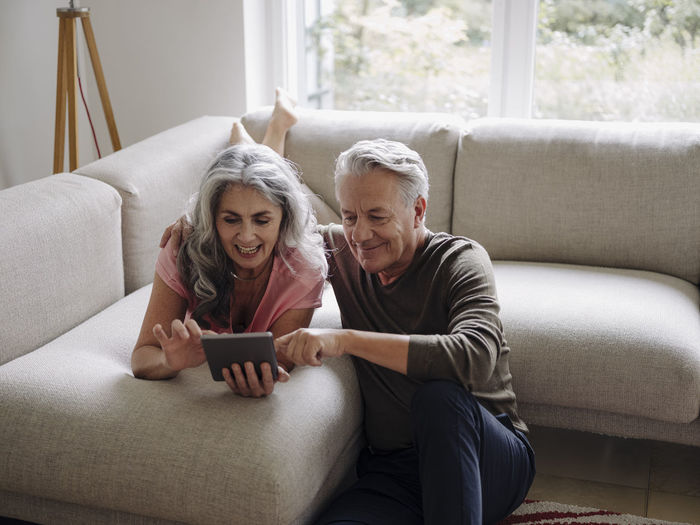 Happy senior couple relaxing on couch at home using tablet