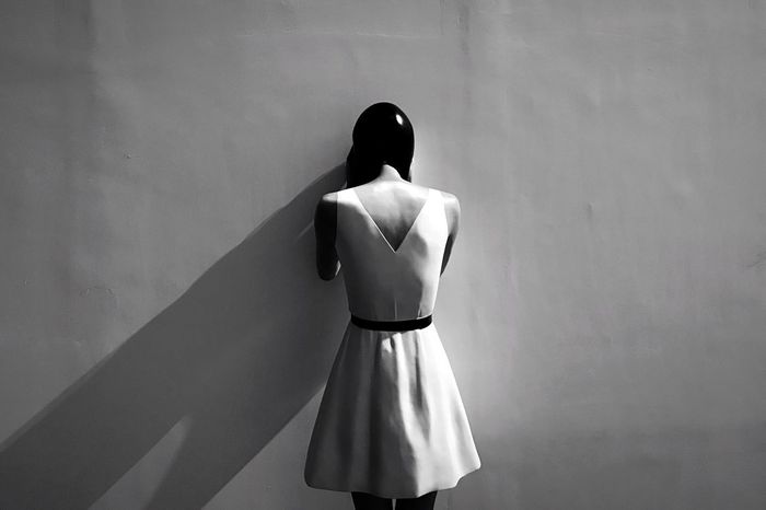 Rear view of woman figurine standing against white wall