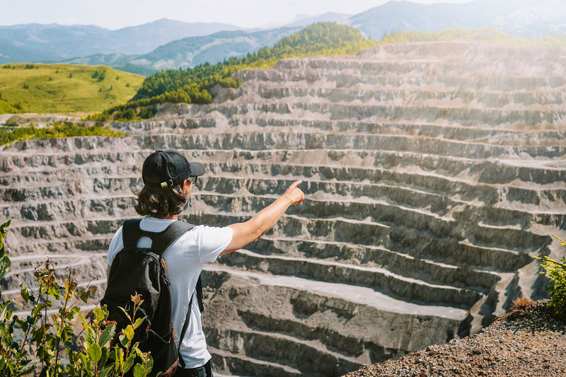 Rear view of man standing on mountain and gesturing to mine open pit