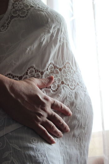 Midsection of pregnant woman standing by window at home