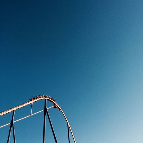 Low angle view of rollercoaster against clear blue sky