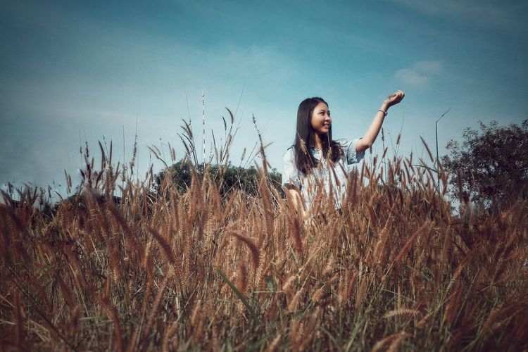 Low angle view of girl holding reed while standing on field against sky