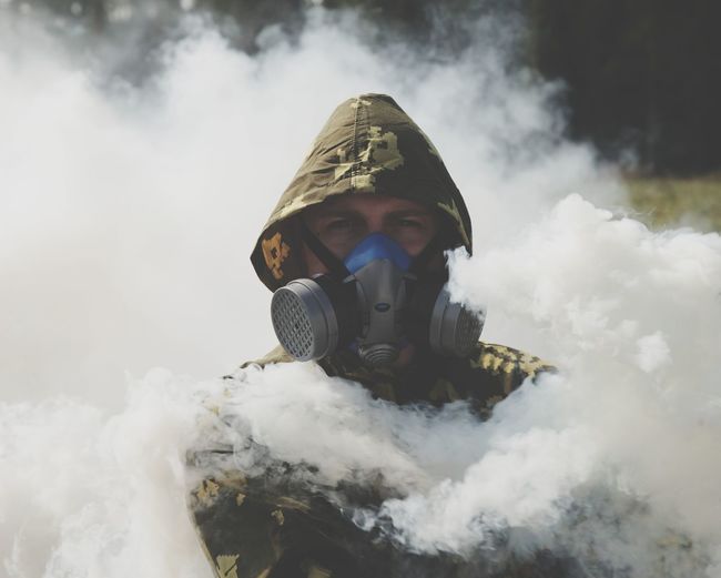 Portrait of young man in gas mask standing amidst smoke