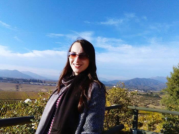 Portrait of young woman wearing sunglasses standing against mountain