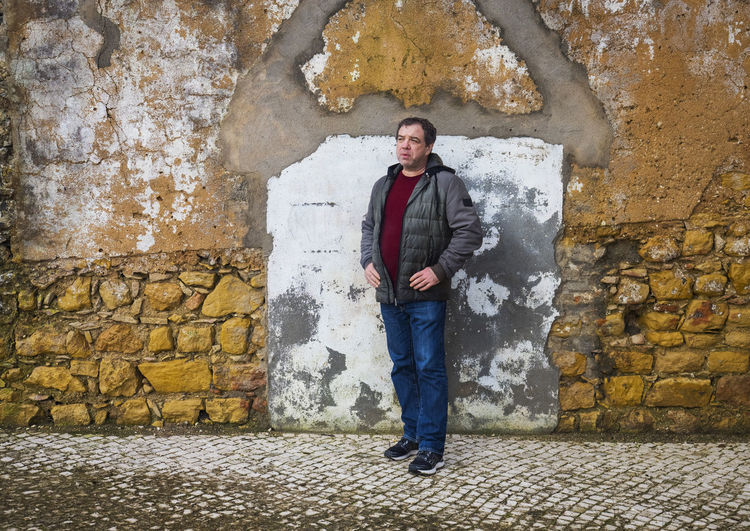 Adult man in a jacket and jeans near an old brick wall