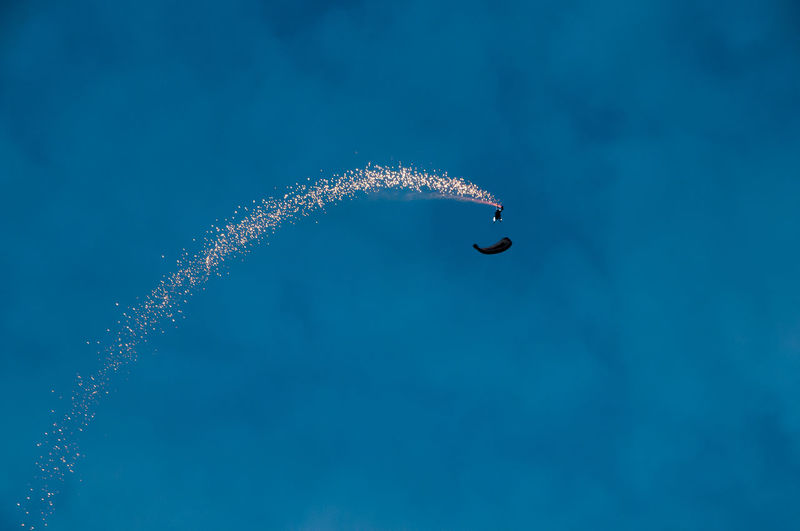 Low angle view of spark by upside down paraglider against blue sky