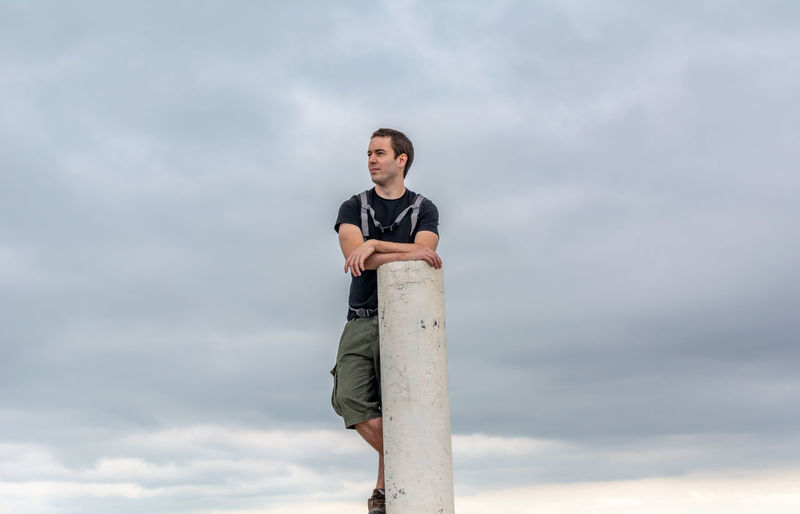 Young man standing by pole against sky