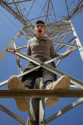 Low angle view of boy sitting on column against sky