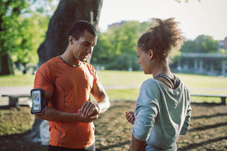 Man showing wristwatch to female friend while standing in park