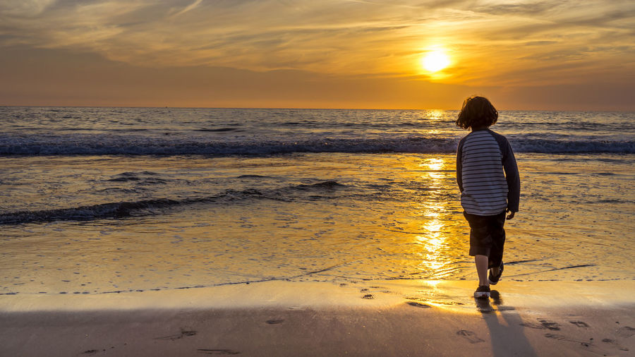 Rear view of boy walking at beach during sunset