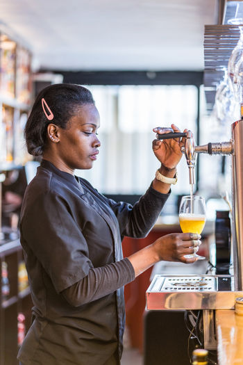 Side view of black female barkeeper pouring cold beer in glass in bar