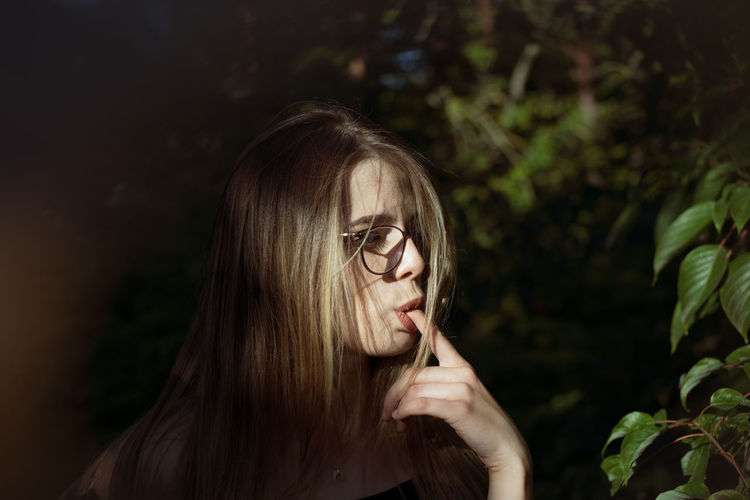 Close-up of woman with finger in mouth standing by plants outdoors