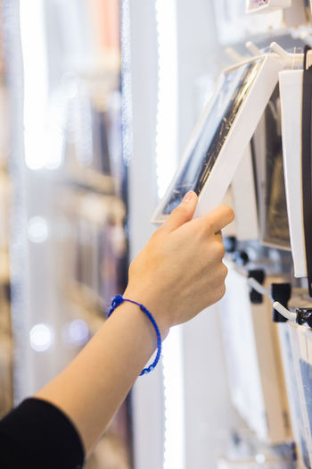 Hand of young female customer holding phone cover box hanging from rack at store