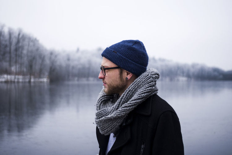 Young man looking away against lake and sky during winter