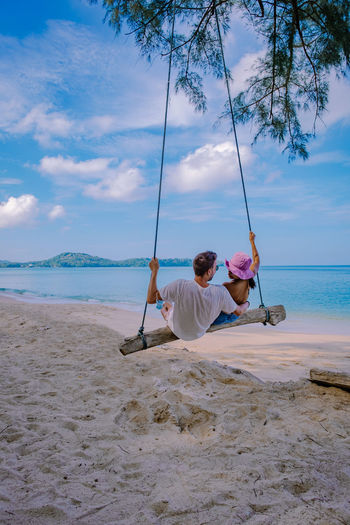 Man sitting on swing at beach against sky