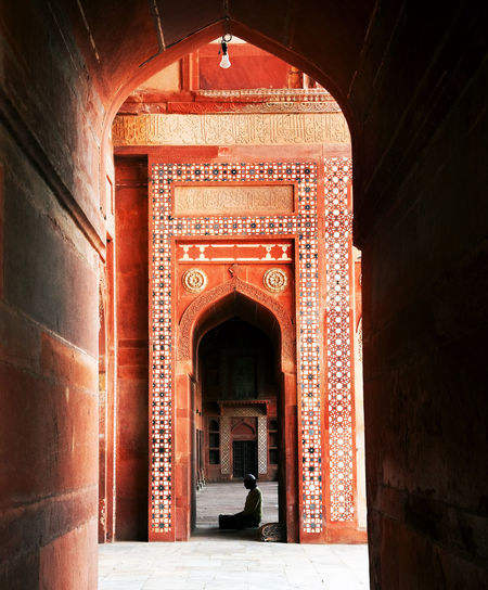 Man praying at jama masjid seen through arch
