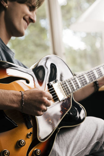 Hand of smiling man playing chord on guitar at home