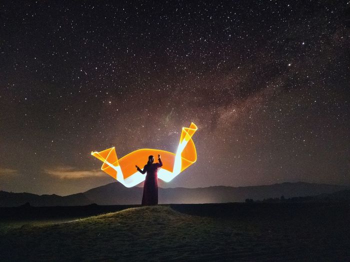 Person standing by umbrella against sky at night