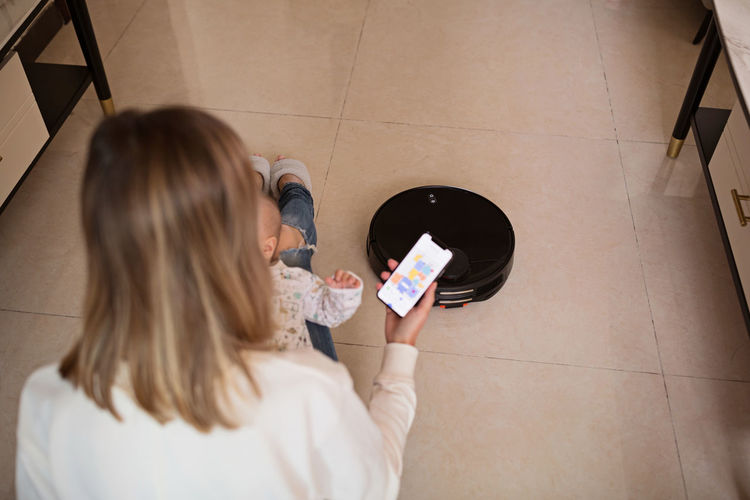 High angle view of mother holding phone while sitting with daughter on floor