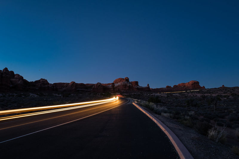 Light trails on road against clear blue sky