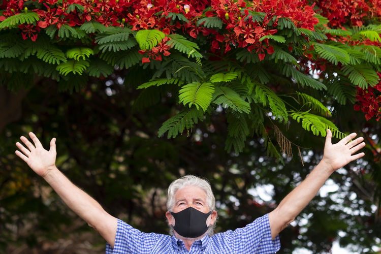 View of senior man with arms outstretched standing by tree outdoors