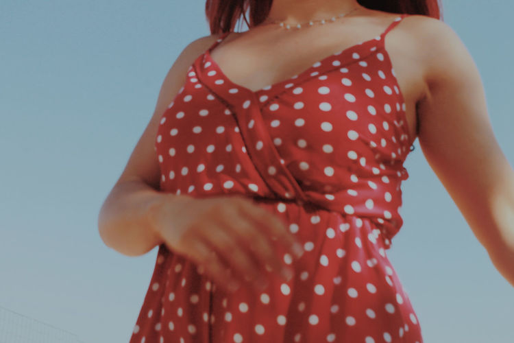 Midsection of woman wearing red dress standing against clear sky