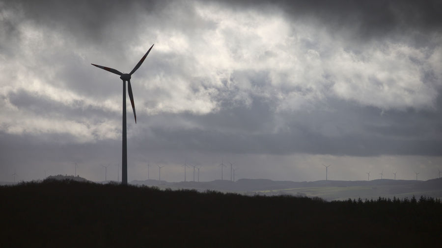 Silhouette wind turbines on field against sky