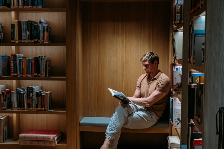 Portrait of a college student man in library. casual clothed guy reading book in bookstore.