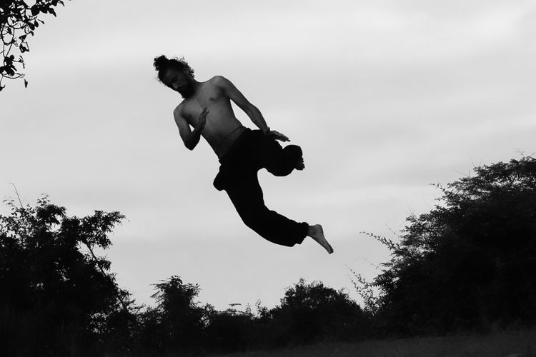 Low angle view of silhouette man jumping against sky