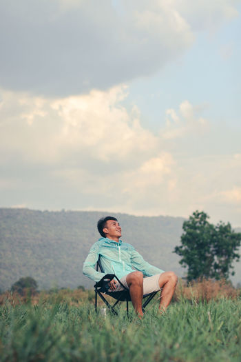 Man sitting on field against sky