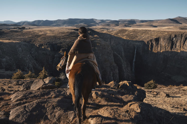 Rear view of woman riding horse on mountain against clear sky