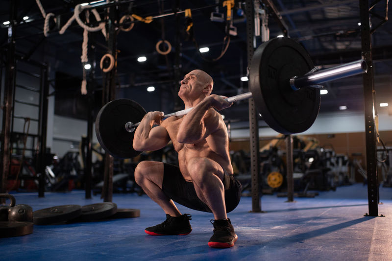 Muscular male athlete squatting with heavy barbell