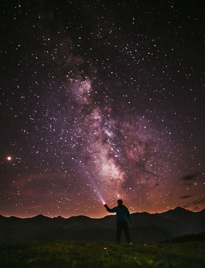 Silhouette person holding illuminated flashlight while standing against starry sky at night